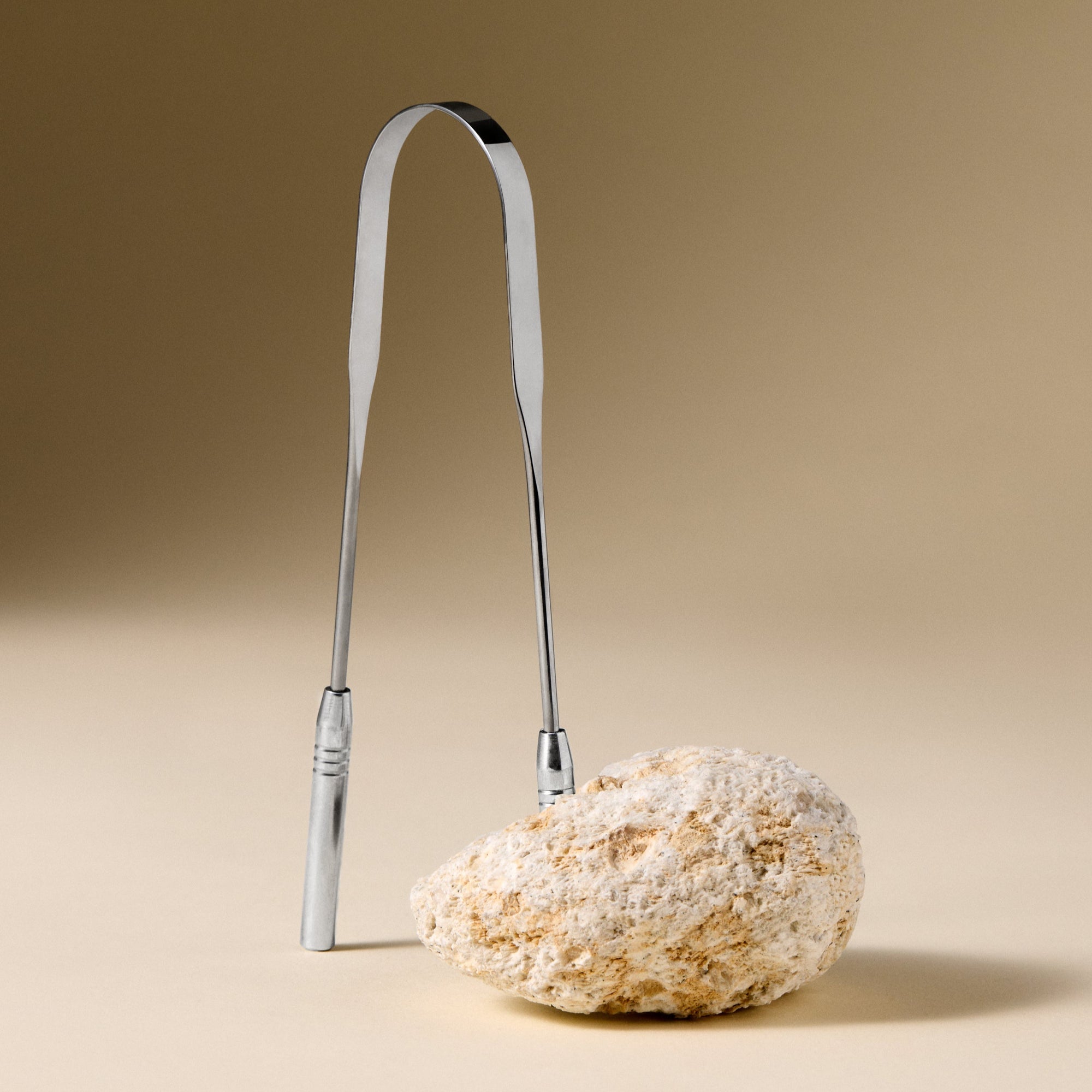 Metallic tounge scraper on a textured beige surface