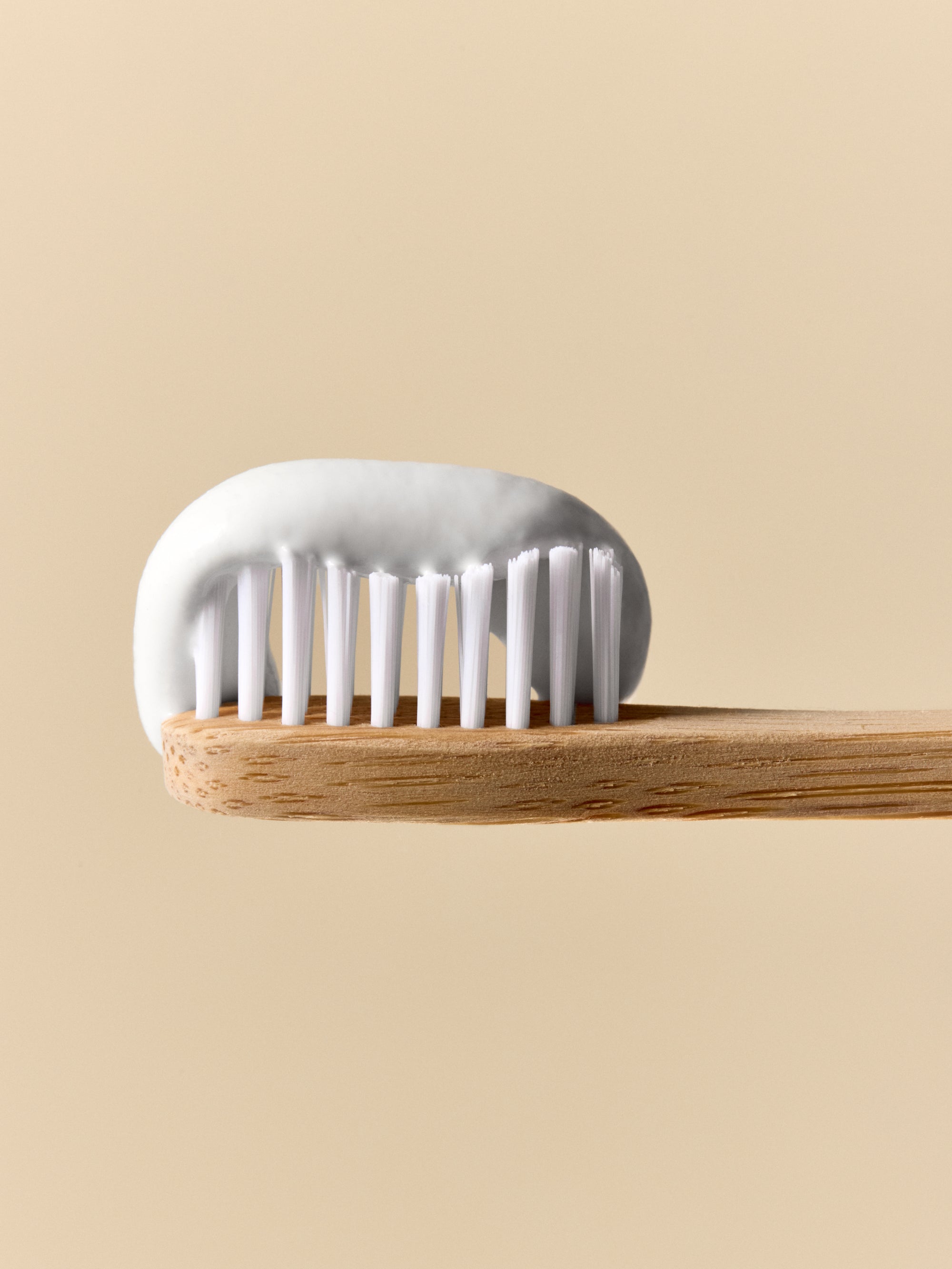 A glass jar filled with toothpaste on a toothbrush, against a beige background.