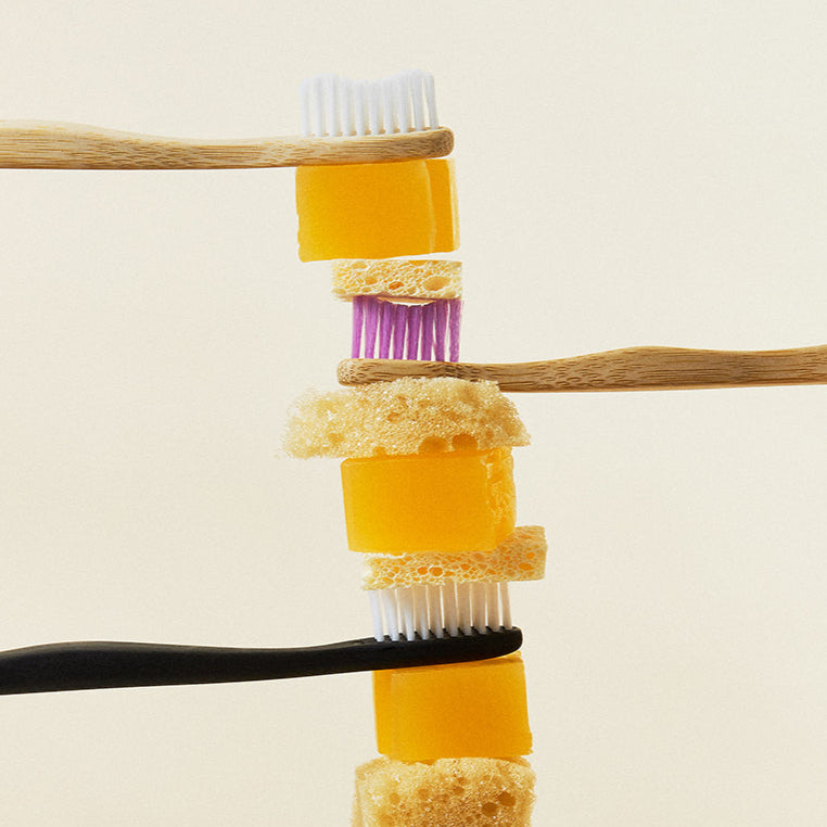 Stack of toothbrushes and toothpaste cubes against a plain background
