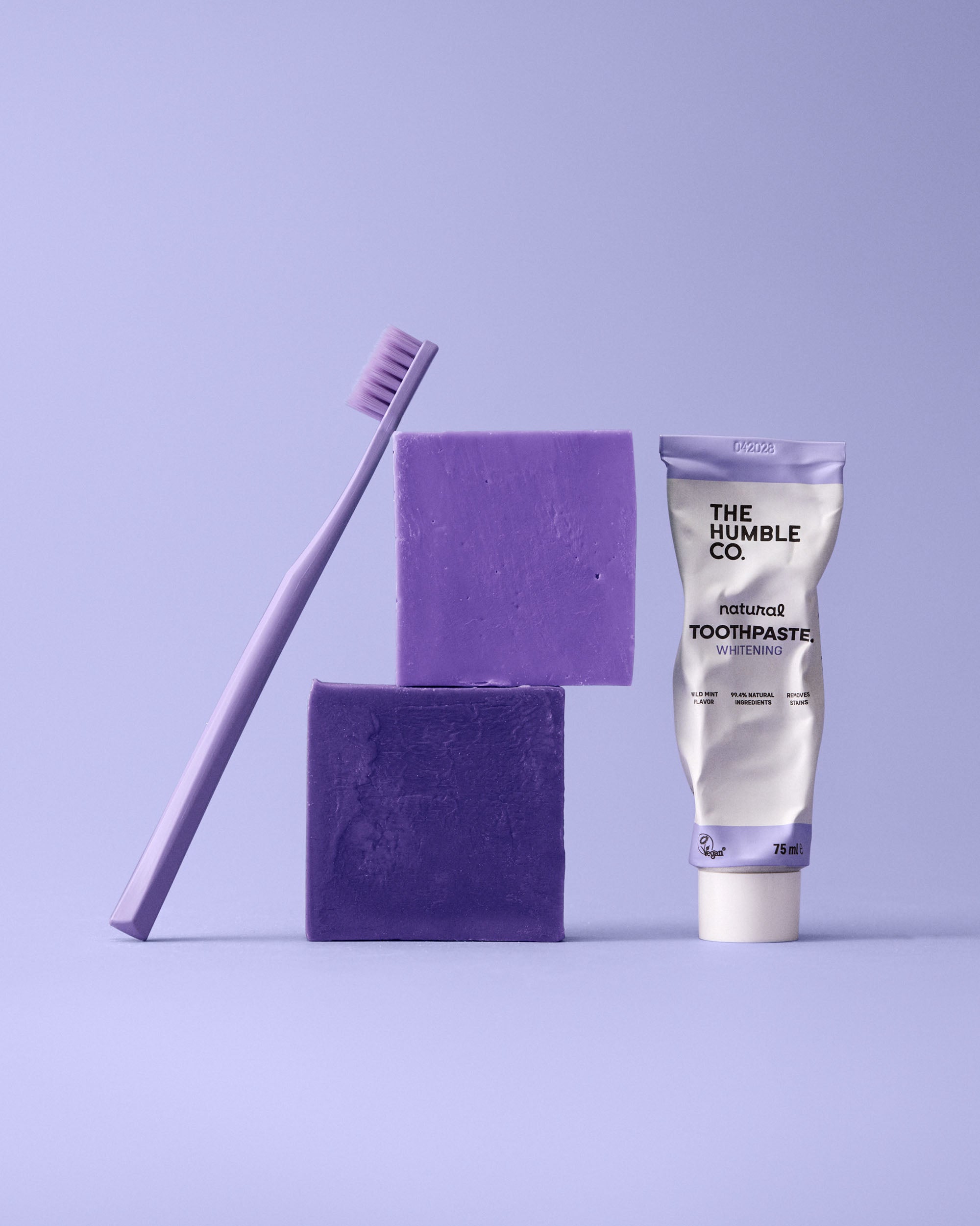 Purple 7k toothbrush, whitening toothpaste, and sponges on a light purple background