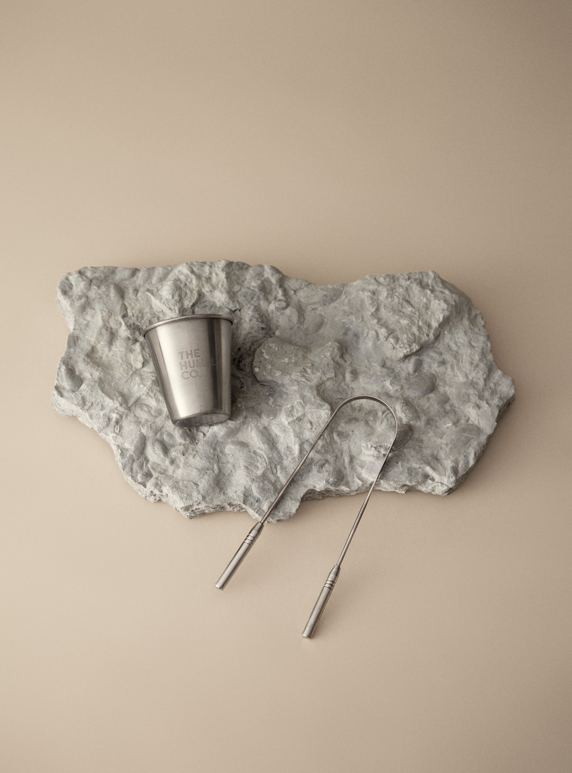 Metal cup and skewer on a textured stone surface against a beige background.