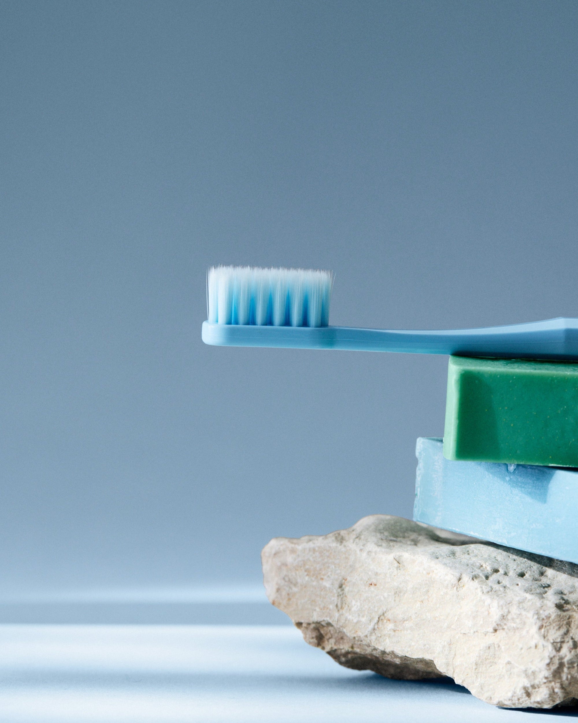 Blue toothbrush and toothpaste on a rock with a gray background