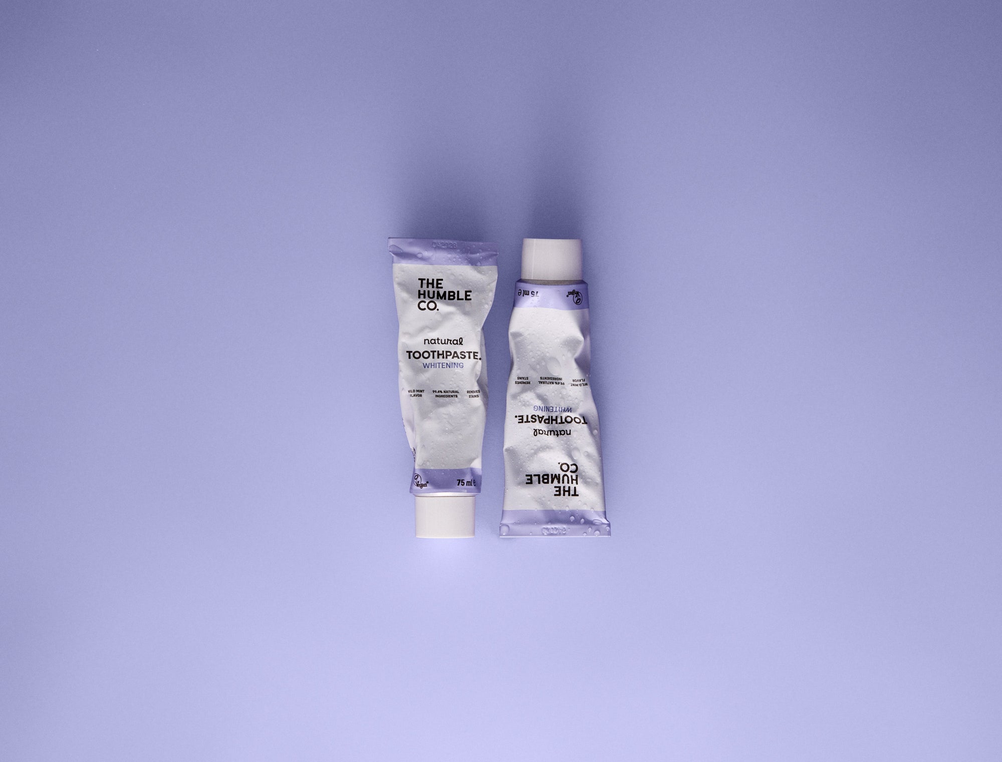Two tubes of toothpaste on a purple background