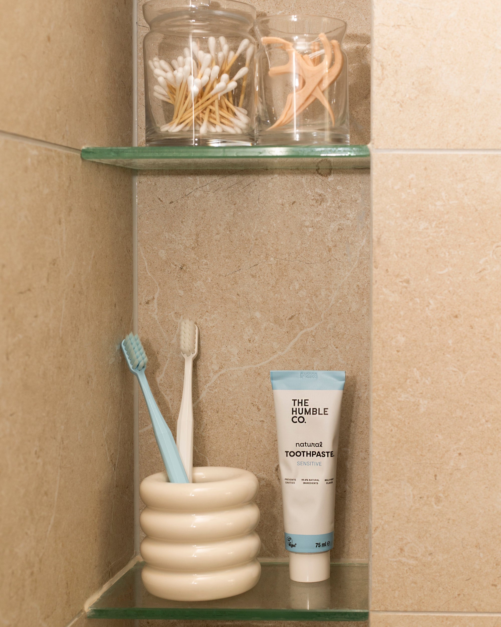 Toothbrush, toothpaste, and containers on a glass shelf in a bathroom.