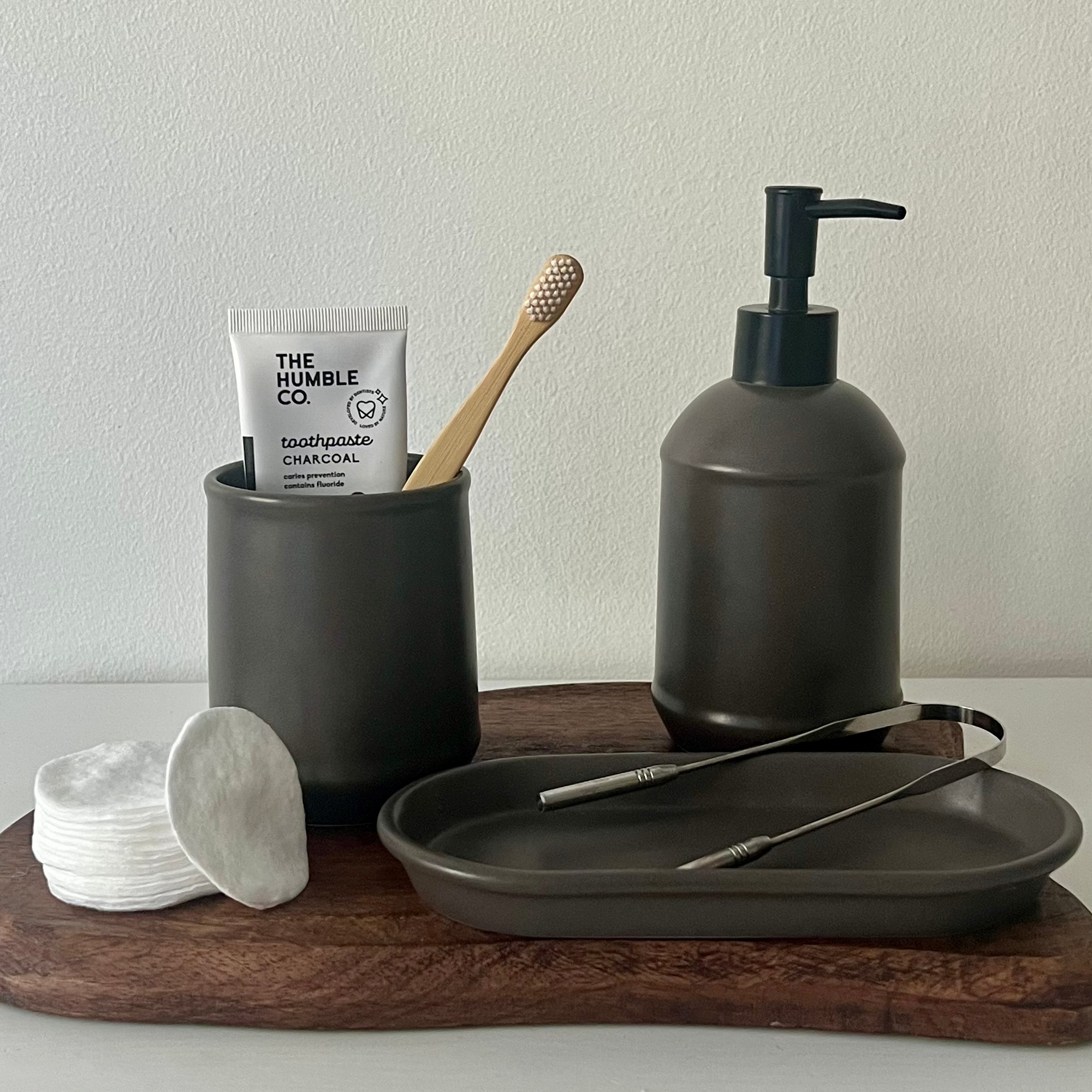 Bathroom essentials including a toothbrush, toothpaste, and soap dispenser on a wooden tray.