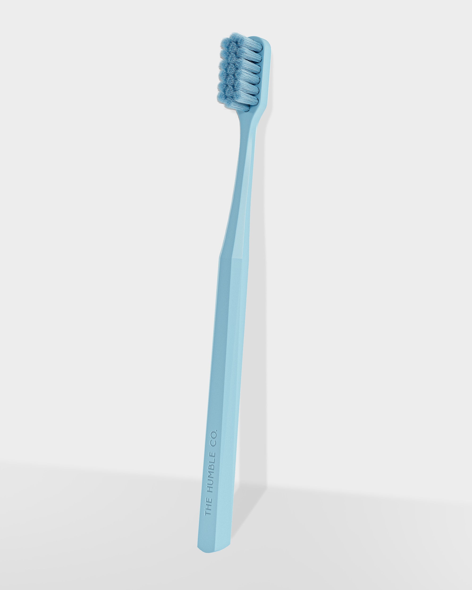 A blue manual toothbrush with a hexagonal handle, standing upright against a white background.