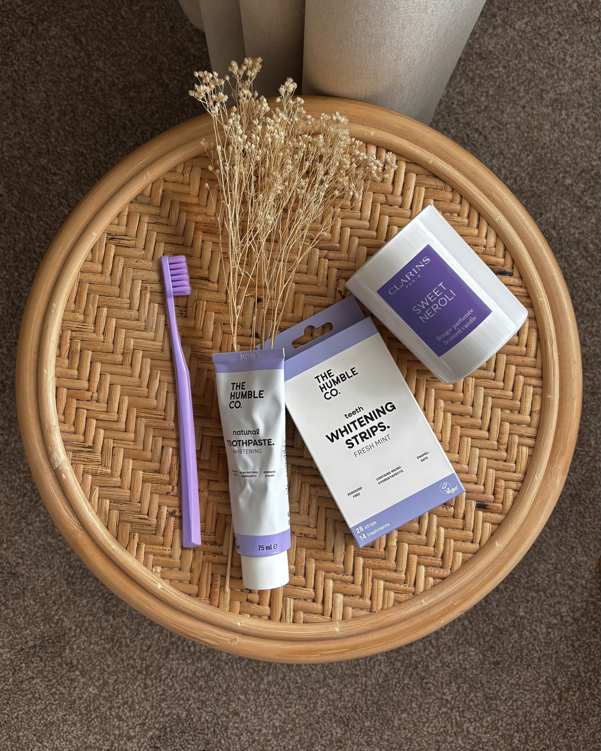 Toothbrush, toothpaste, whitening strips, and sweetener on a woven tray with a neutral background
