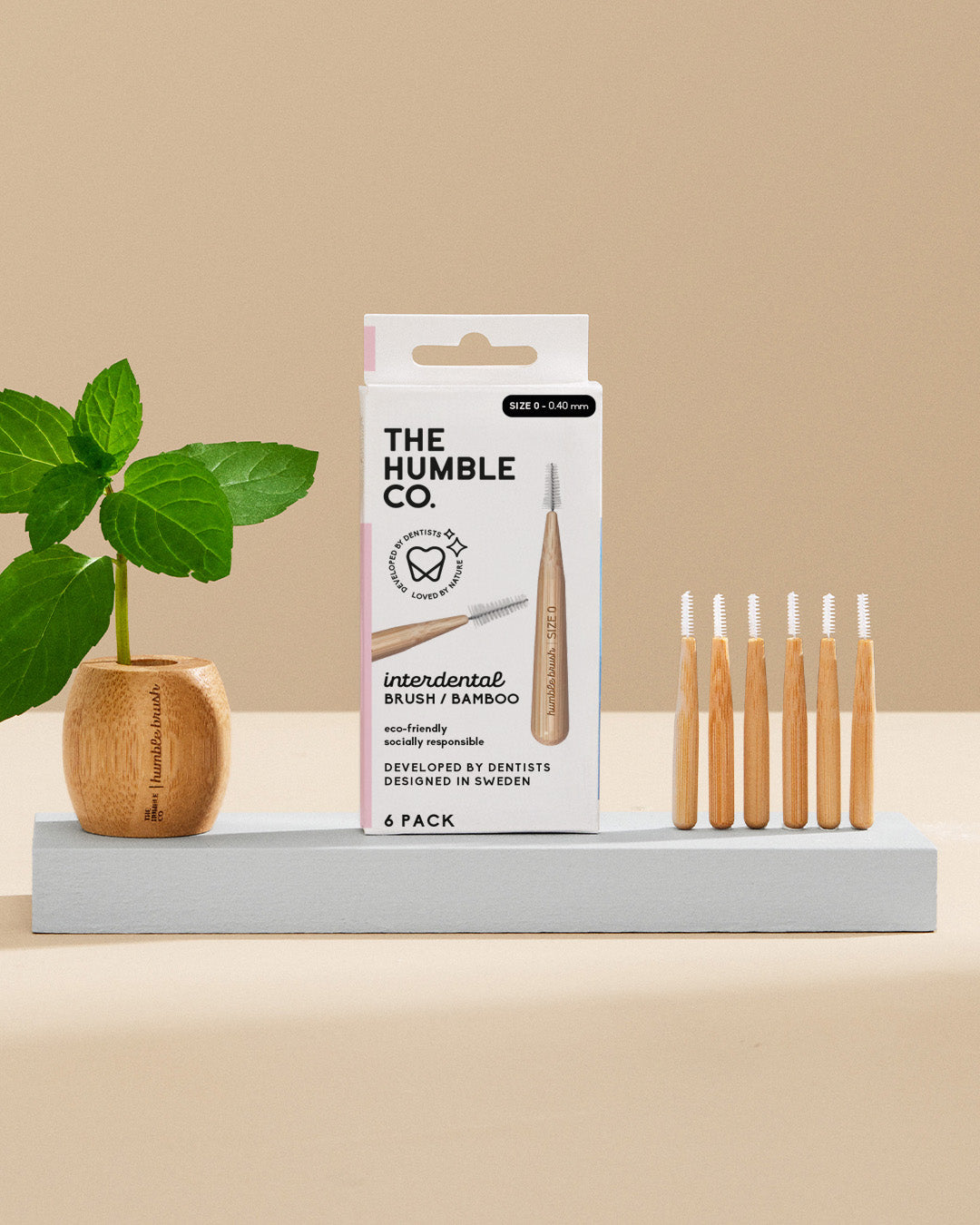 Packaging and multiple interdental brushes with bamboo handles displayed on a platform, with a plant in the background.