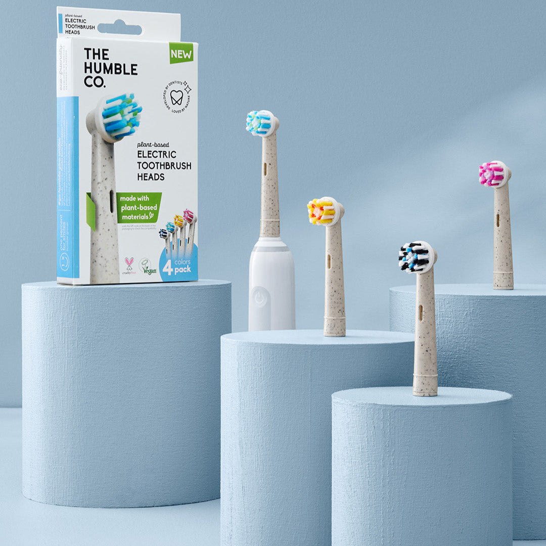 Electric toothbrush heads on cylindrical stands with packaging labeled 'The Humble Co.' against a light blue background.
