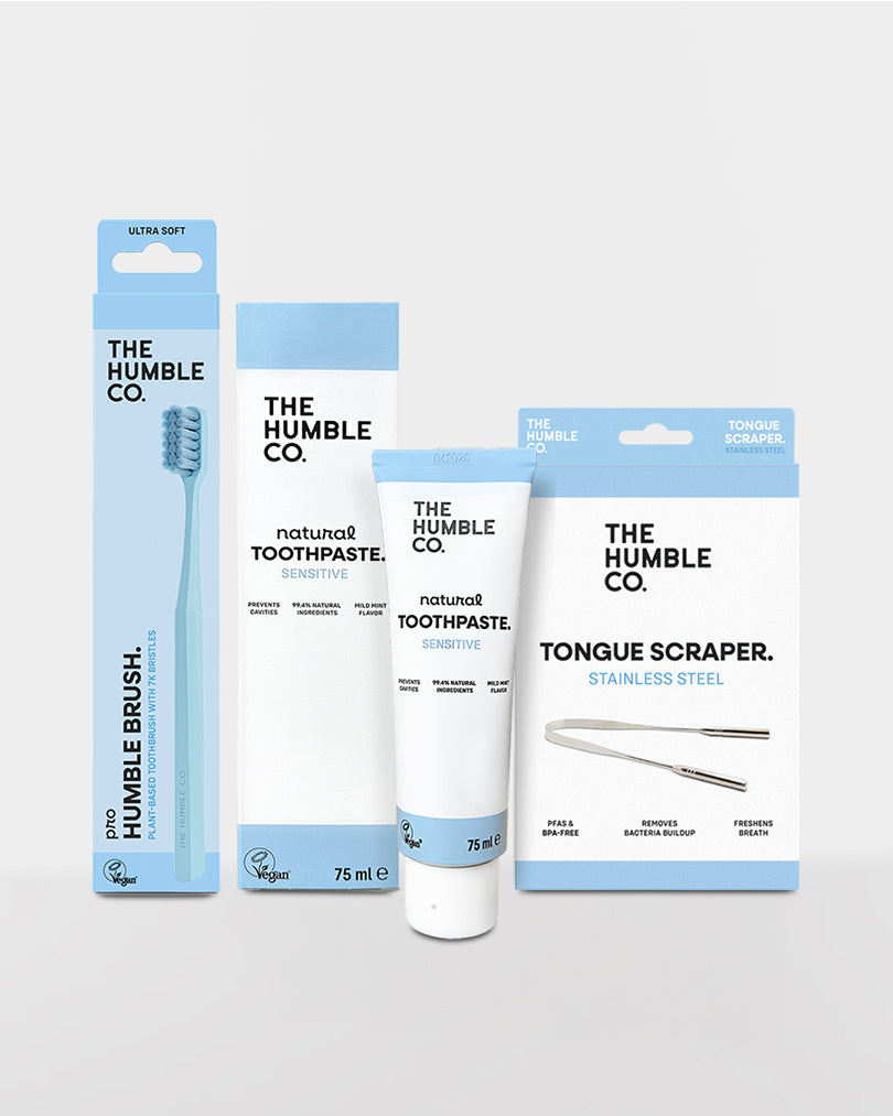 Collection of The Humble Co. dental care products including a toothbrush, toothpaste, and tongue scraper on a light gray background.