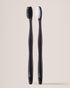 Two black toothbrushes with white bristles on a beige background
