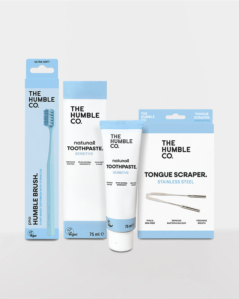 Collection of The Humble Co. dental care products including a toothbrush, toothpaste, and tongue scraper on a light gray background.