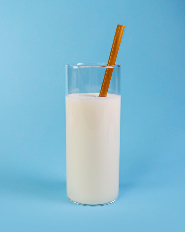 A refreshing glass of milk with a reusable bamboo straw, against a calming blue backdrop, a sustainable choice for sipping your favorite drinks.
