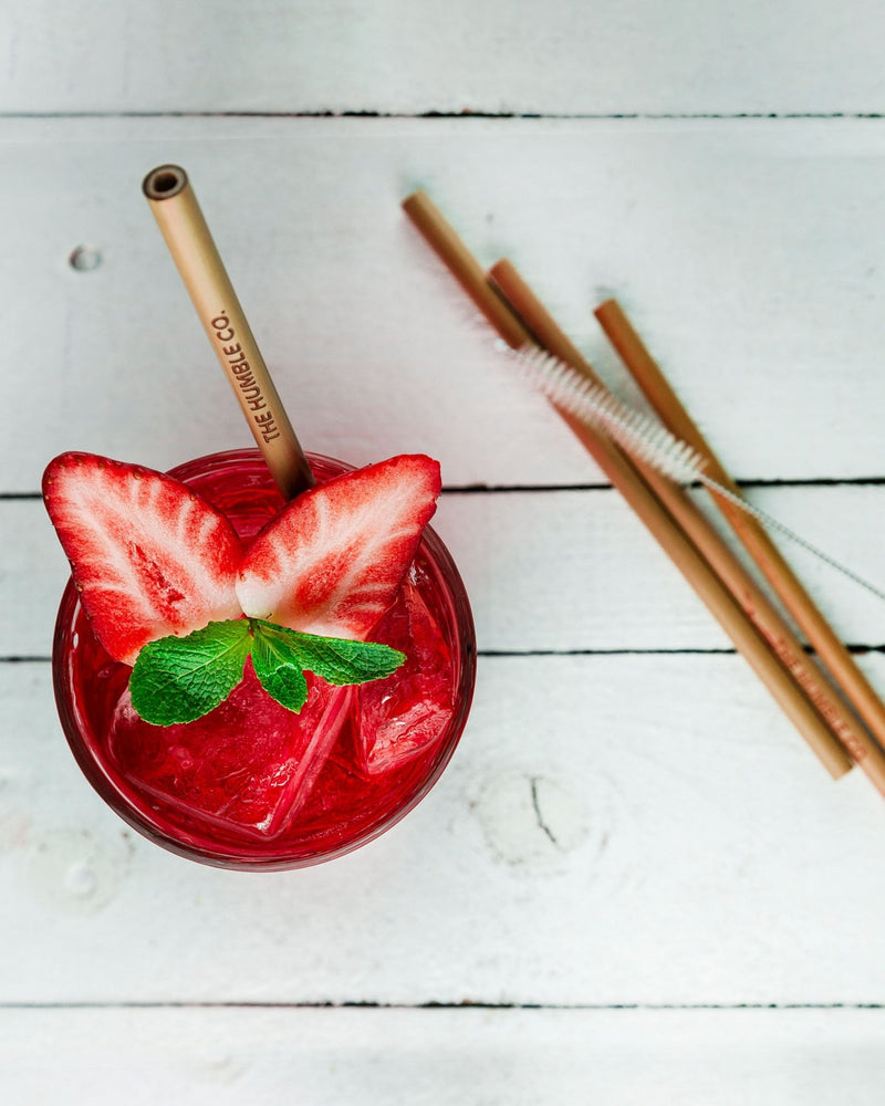 A refreshing strawberry drink topped with mint served in a glass with a reusable bamboo straw, promoting a sustainable and delicious beverage experience.