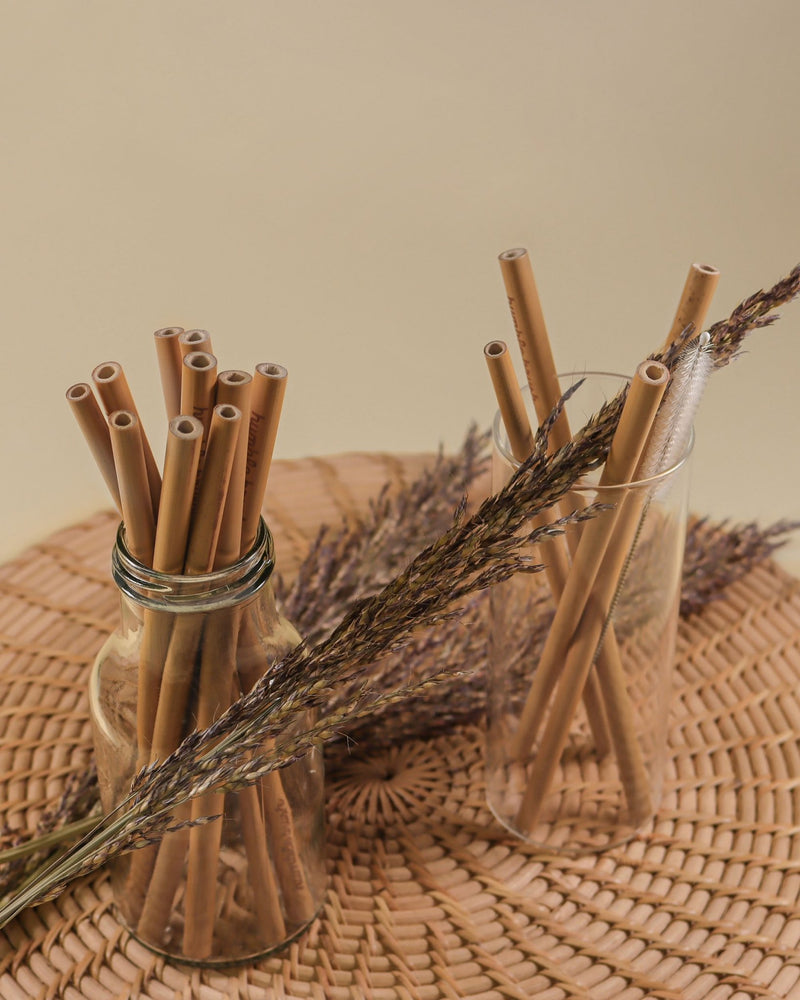 A jar of reusable bamboo straws from The Humble Co. is placed on a wooden table, surrounded by wheatgrass for a natural and sustainable touch.