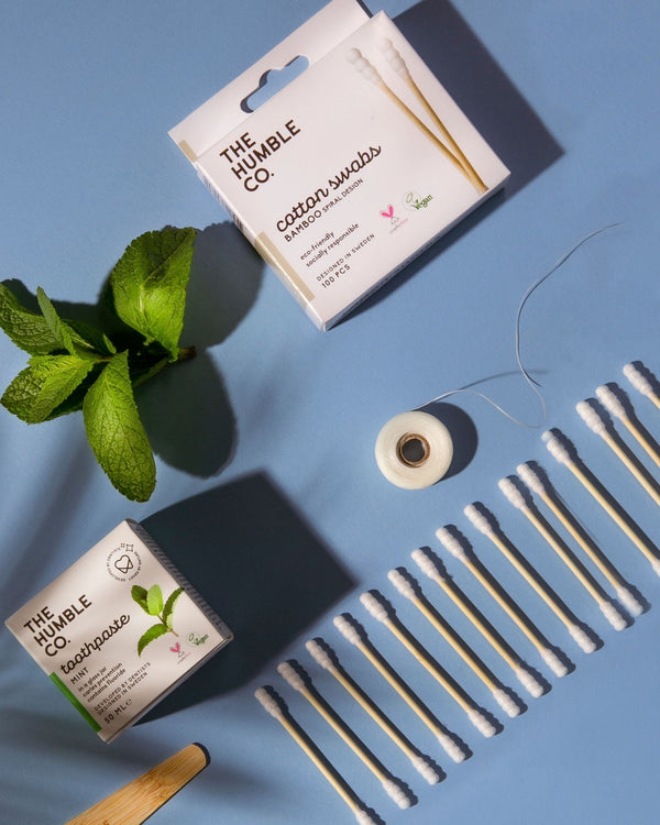 A box of The Humble Co. Bamboo Cotton Swabs and a package and roll of The Humble Co. mint floss, sustainable alternatives to disposable products.