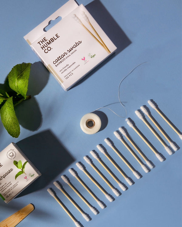 A box of The Humble Co. Bamboo Cotton Swabs and a package and roll of The Humble Co. mint floss, sustainable alternatives to disposable products.